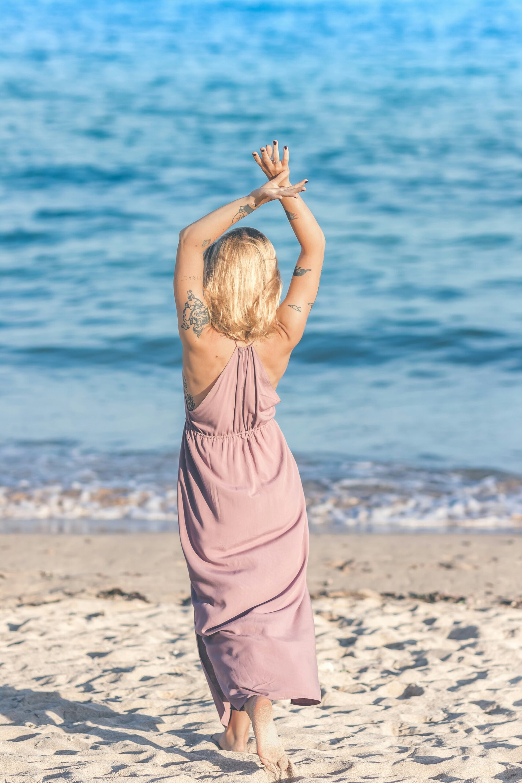 woman wearing pink dress raising both hands while walking on shore